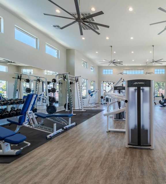 A spacious gym with a variety of equipment and a ceiling fan. at Vistoria At Marley Park Apartments, Arizona