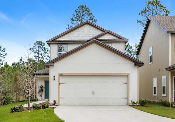 A two-story house with a white garage door and light siding is shown under a partly cloudy sky.