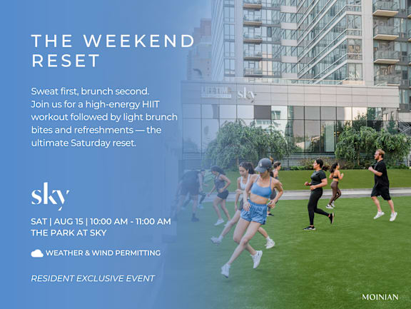 A group of people are running in a park in front of a building with the word "sky" on it.