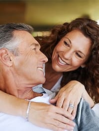 an older man and woman sitting on a couch with their arms around each other