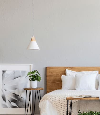A bedroom with a bed, plants, and a picture frame on the wall.