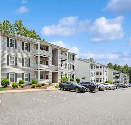 A large white apartment building with a parking lot in front of it.