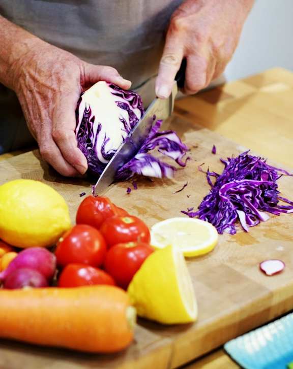 A person is cutting a red cabbage on a wooden cutting board.