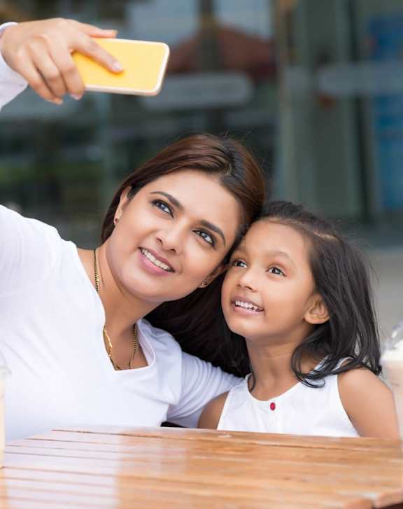 A woman and a child are taking a selfie at a table with shopping bags and drinks.
