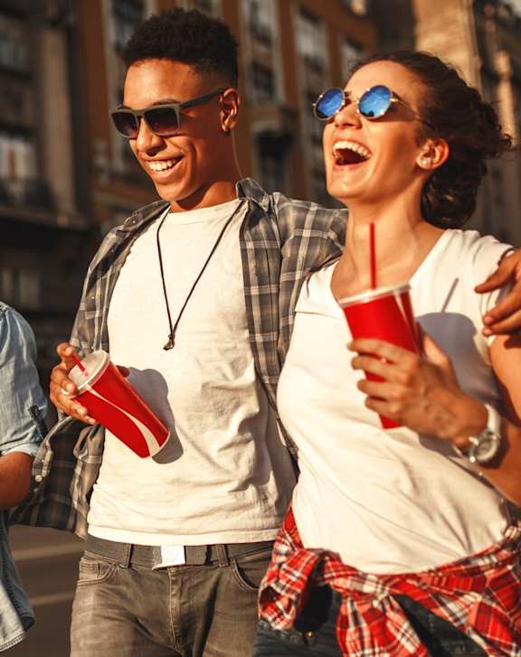 Three friends are walking down the street holding red cups.