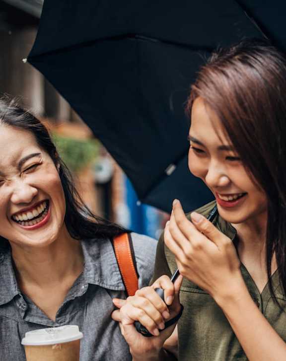 Two women laughing and holding an umbrella.