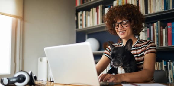 a woman working on her laptop with her dog sitting on her lap