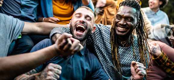 Two people laughing and holding hands in a crowd.