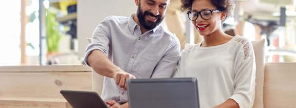 Two people are sitting on a bench and looking at a laptop.