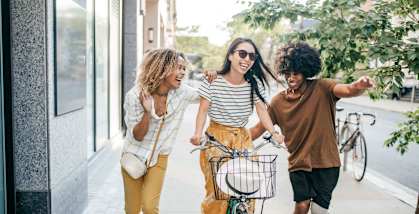 three friends walking a bike down a sidewalk