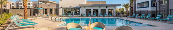  Luxurious apartment complex showcasing a stylish outdoor pool area with cozy wicker seating and a modern fire pit, surrounded by palm trees under a clear blue sky.