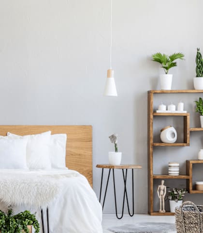 A bedroom with a bed, plants, and a picture frame on the wall.