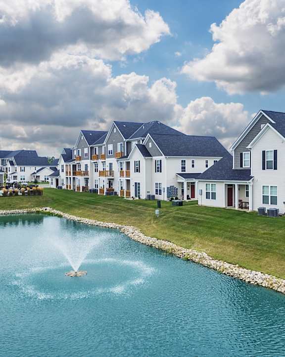 a fountain in the middle of a pond in front of houses