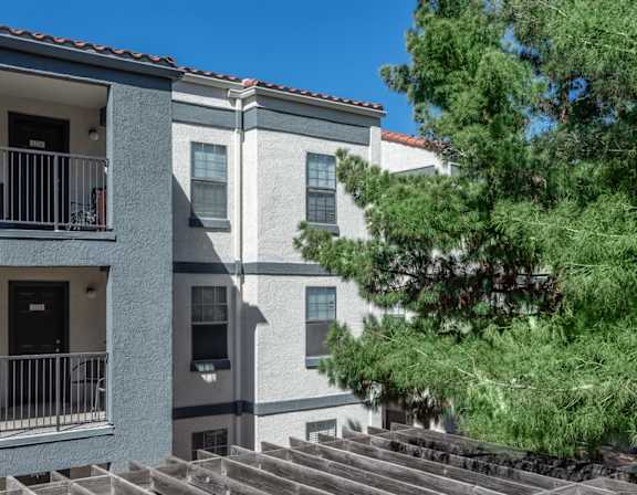 A modern apartment building with a balcony and a tree in front.