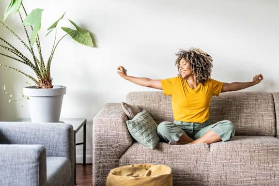 A person in a yellow shirt is sitting on a couch with their arms outstretched.