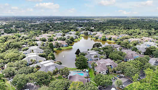 A bird's eye view of a residential area with houses, trees, and a pond.