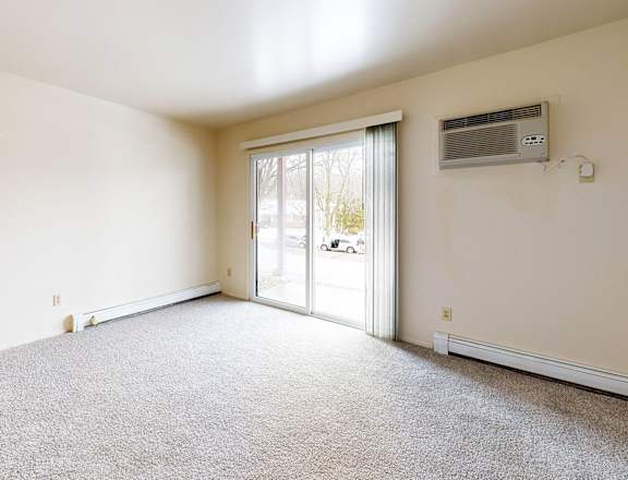 A room with a carpeted floor, a sliding glass door, and a wall-mounted air conditioning unit.