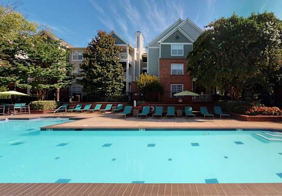 a swimming pool with lounge chairs and umbrellas in front of a brick building at Autumn Park Apartments, Charlotte, NC, 28262