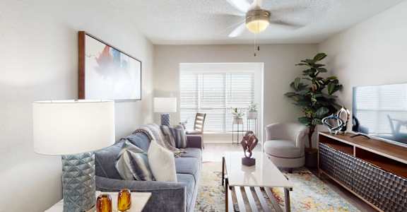 A living room with a grey couch, a white coffee table, a ceiling fan, and a painting on the wall.