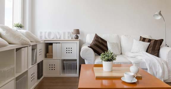 A white couch with brown pillows and a wooden coffee table with a plant on it.