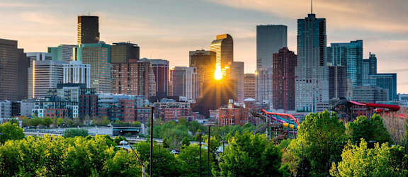 A city skyline at sunset with the sun setting behind the buildings.
