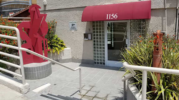 A red sculpture resembling a heart stands in front of a building with a red awning and the number 1156.