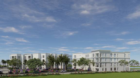 A modern building with white walls and balconies is surrounded by greenery and trees.