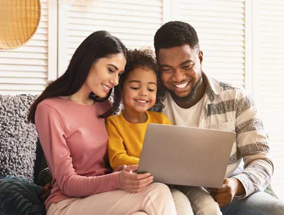 A family of three is sitting on a couch with a laptop.