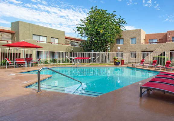 A pool with red chairs and umbrellas in front of a building.