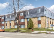 Thumbnail 1 of 8 - a brick apartment building with two cars parked in front