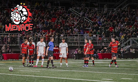 A group of soccer players in red and white uniforms are lined up on the field with a logo that reads "MENACE" above them.