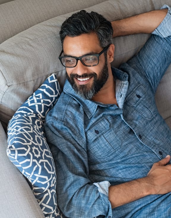 a man with glasses and a blue shirt is laying on a couch