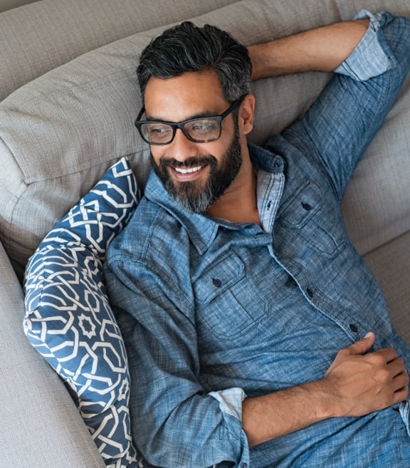 a man with glasses and a blue shirt is laying on a couch