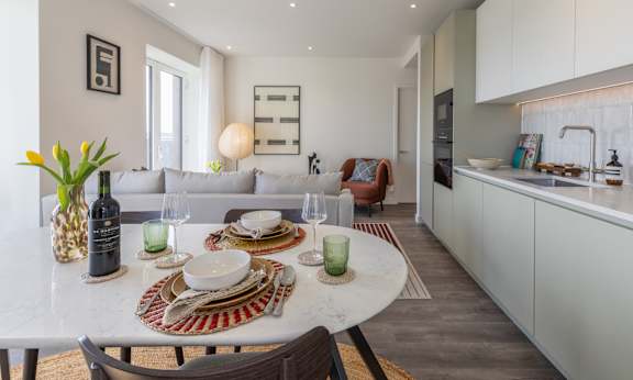 A dining table set with plates and glasses is in the foreground of a modern kitchen.