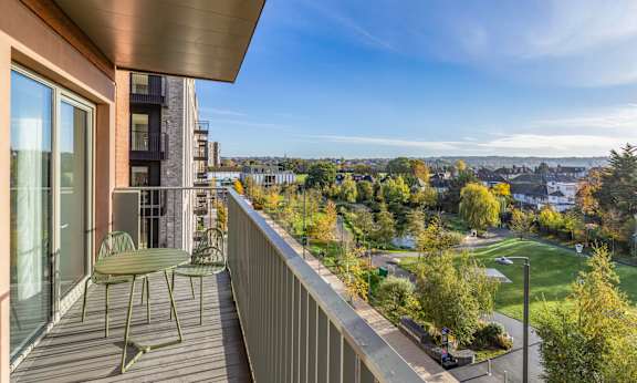 A balcony with a table and chairs overlooks a park and buildings.