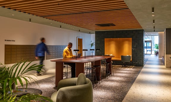 A man walks past a long table with chairs and a plant in a modern room.