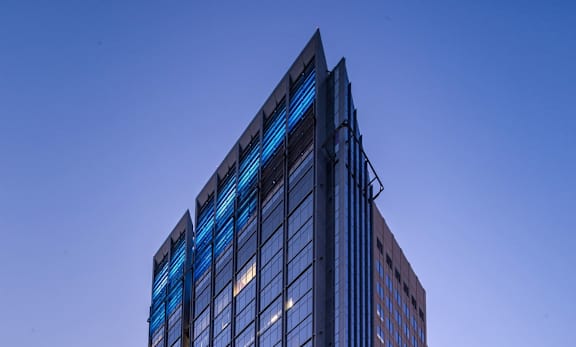 A tall building with blue glass windows stands in the evening sunlight.
