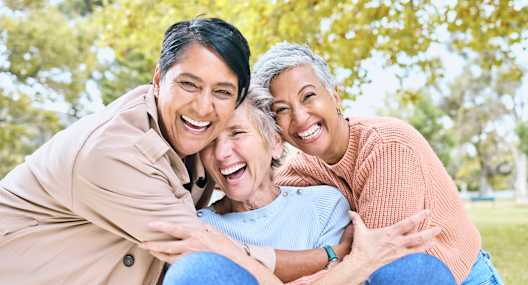 a man and two women sitting in a park with their arms around each other