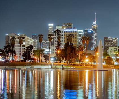 A cityscape at night with a fountain in the foreground.