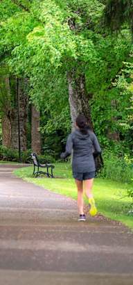 A woman in a black jacket and yellow pants walks down a tree-lined path.