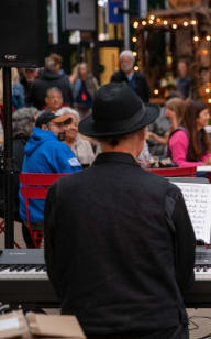 a woman standing in front of a keyboard and a man playing a piano in front