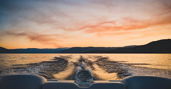 A boat is seen from the back with a beautiful sunset in the background.