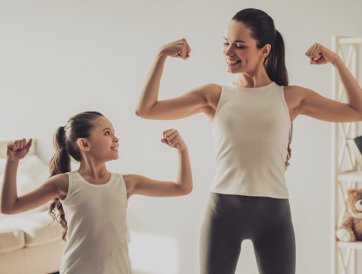 A woman and a girl flexing their biceps in a room.