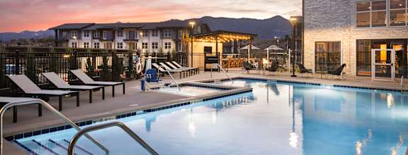 a swimming pool at dusk with a building and mountains in the background