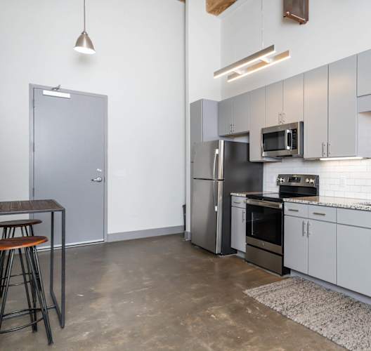 Industrial-style kitchen with high ceilings, white cabinets, and stainless steel appliances.