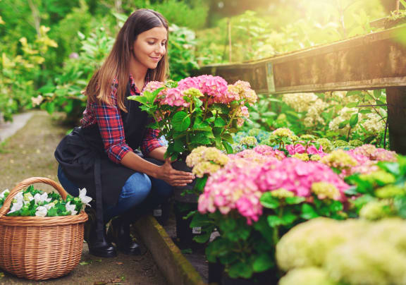 a woman crouching in a garden with a basket of flowers