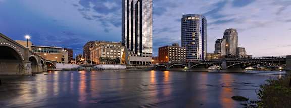 A tall skyscraper next to a river with a bridge in Grand Rapids, Michigan