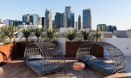 Two metal wire chairs on a wooden deck with a city skyline in the background.