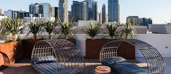 Two metal wire chairs on a wooden deck with a city skyline in the background.