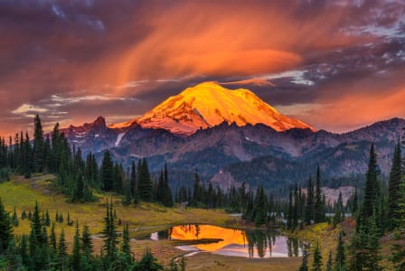 a fiery sunset over mount rainier with a lake in the foreground